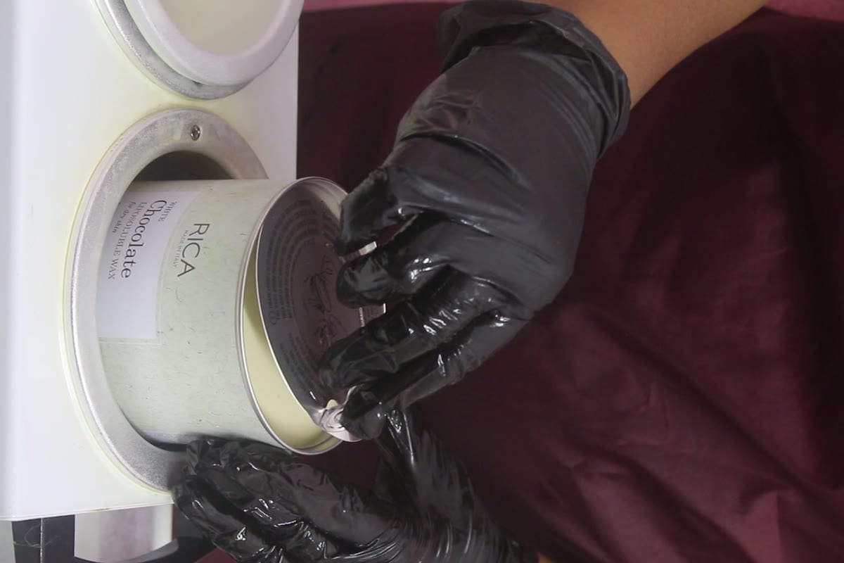 Gloved hands placing a fresh RICA wax tin into the warmer — single-brand premium wax